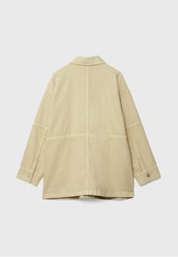 béžová, oversized bunda vyrobená z bavlny s jemnou texturou. Má klasický límeček, knoflíkové manžety a švy podél zadní strany.