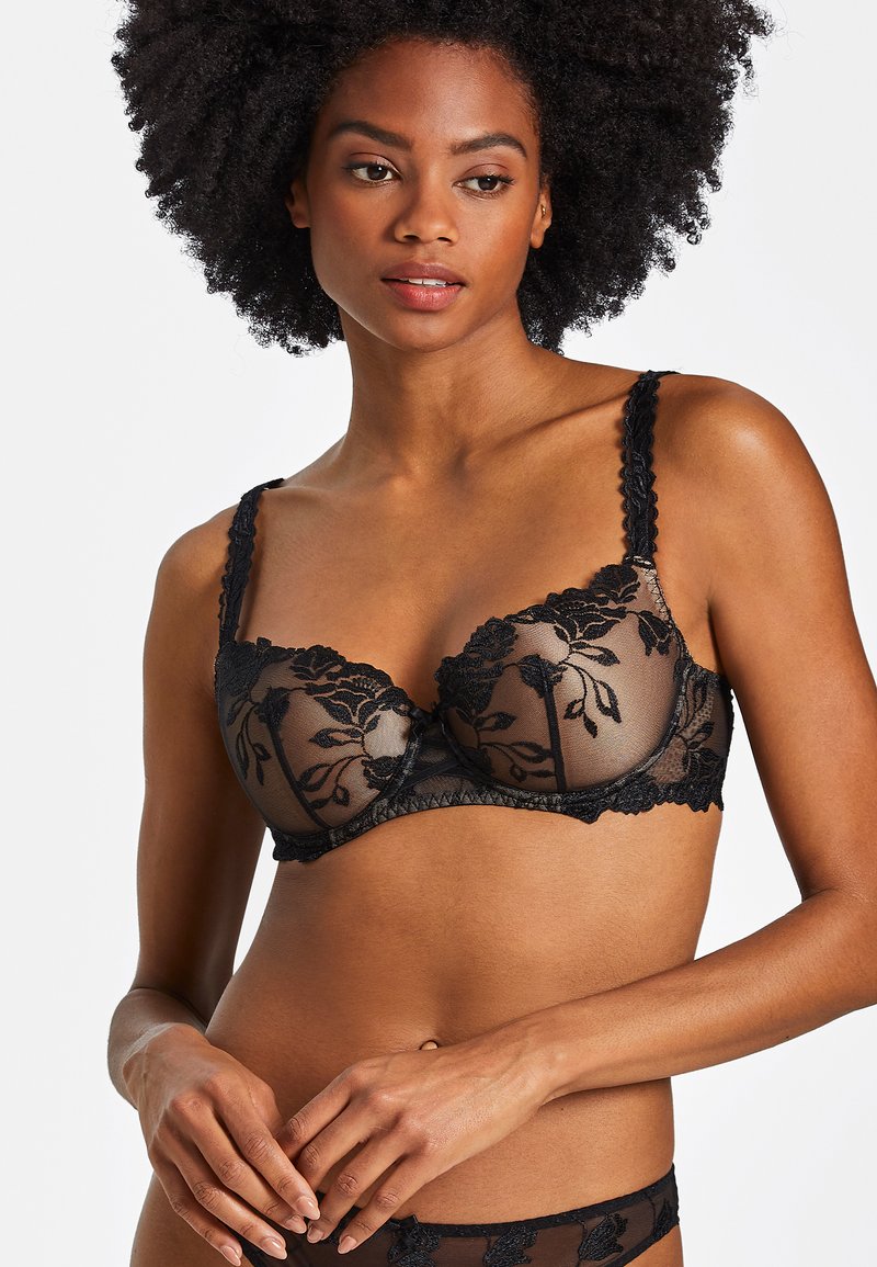 Soutien-gorge en dentelle noire avec des panneaux transparents, broderie florale, bords festonnés et bretelles ajustables. La dentelle texturée ajoute du détail.