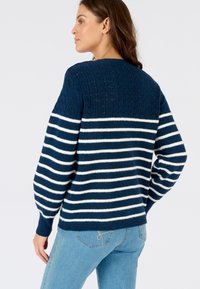 Jersey de punto azul marino con rayas horizontales blancas, con un yugo texturizado y mangas ligeramente abullonadas. Combinado con jeans de color azul claro.