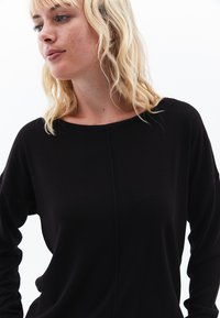 Top nero a maniche lunghe con scollatura rotonda e vestibilità rilassata. Realizzato in un tessuto morbido e liscio, presenta dettagli di cucitura discreti.