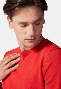 Czerwony sweter dziany z okrągłym dekoltem, z prążkowanymi mankietami i dolnym wykończeniem. Mały detal logo na lewej piersi. Miękka faktura.