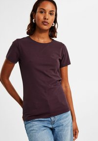 Pflaumenfarbenes T-Shirt mit kurzen Ärmeln und Rundhalsausschnitt, aus weichem Stoff, figurnaher Schnitt, kombiniert mit hellblauen Jeans.