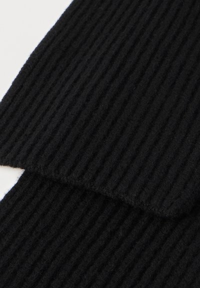 Svart ribbad trikåtyg med vertikala mönster och en mjuk struktur. Kanterna är prydligt avslutade, vilket visar en modern design.