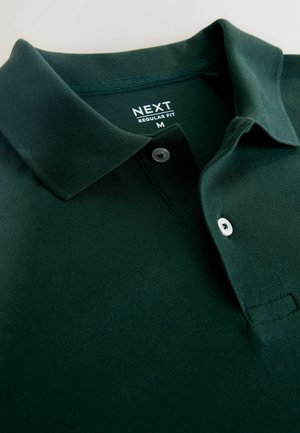 Polo de color verde oscuro hecho de algodón texturizado. Cuenta con un cuello clásico, una tapeta de dos botones y una etiqueta tejida de la marca en el cuello.