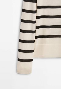 Pull rayé dans des tons beige et noir, avec une texture douce, des poignets côtelés et un design décontracté. Les rayures sont régulièrement espacées.