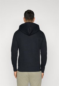 Sweatshirt preto com capuz arredondado, mangas longas, punhos e barra canelados; apresenta uma textura suave e um design minimalista.
