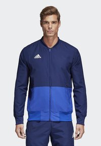 Blaues und marineblaues, zip-up Sportjacke mit geripptem Kragen und Bündchen. Mit Adidas-Logo auf der linken Brust und seitlichen Reißverschlusstaschen.