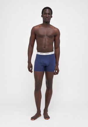 Marineblaue Boxershorts mit einem weißen elastischen Bund, auf dem ein Logo der Marke zu sehen ist. Glatte Textur, taillierte Passform und Oberschenkellänge.