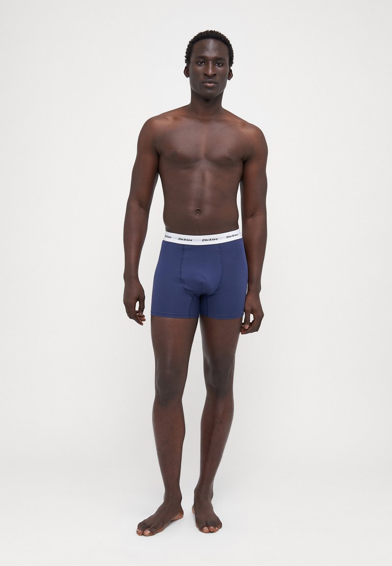 Marineblaue Boxershorts mit einem weißen elastischen Bund, auf dem ein Logo der Marke zu sehen ist. Glatte Textur, taillierte Passform und Oberschenkellänge.