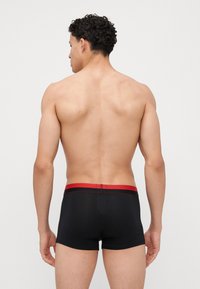 Black boxer briefs with a red waistband featuring a thin accent line, made from a smooth, stretchy material, displayed from the back.