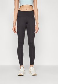 Leggings noirs avec une taille haute, design sans couture et accents cousus. Associés à des chaussures de sport blanches.
