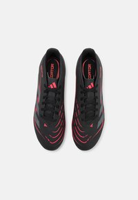 Baskets de sport noires avec une surface texturée, présentant des accents rouges et des motifs rayés. Comprend des lacets noirs et un col rembourré.
