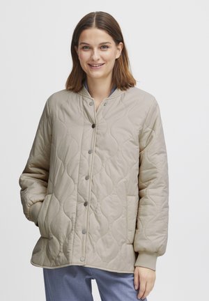 Veste matelassée beige avec un col rond, des boutons-pression, des poches latérales et des poignets côtelés. Tissu lisse et léger avec une texture souple.