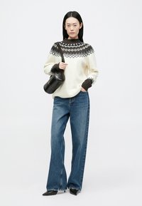 Cream knit sweater with dark collar and geometric pattern, paired with wide-leg blue jeans and a round black handbag. Smooth texture.