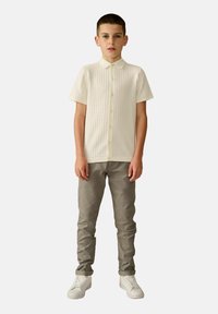 Chemise à manches courtes, crème, avec un tissu texturé, associée à un pantalon gris slim-fit et des baskets blanches.