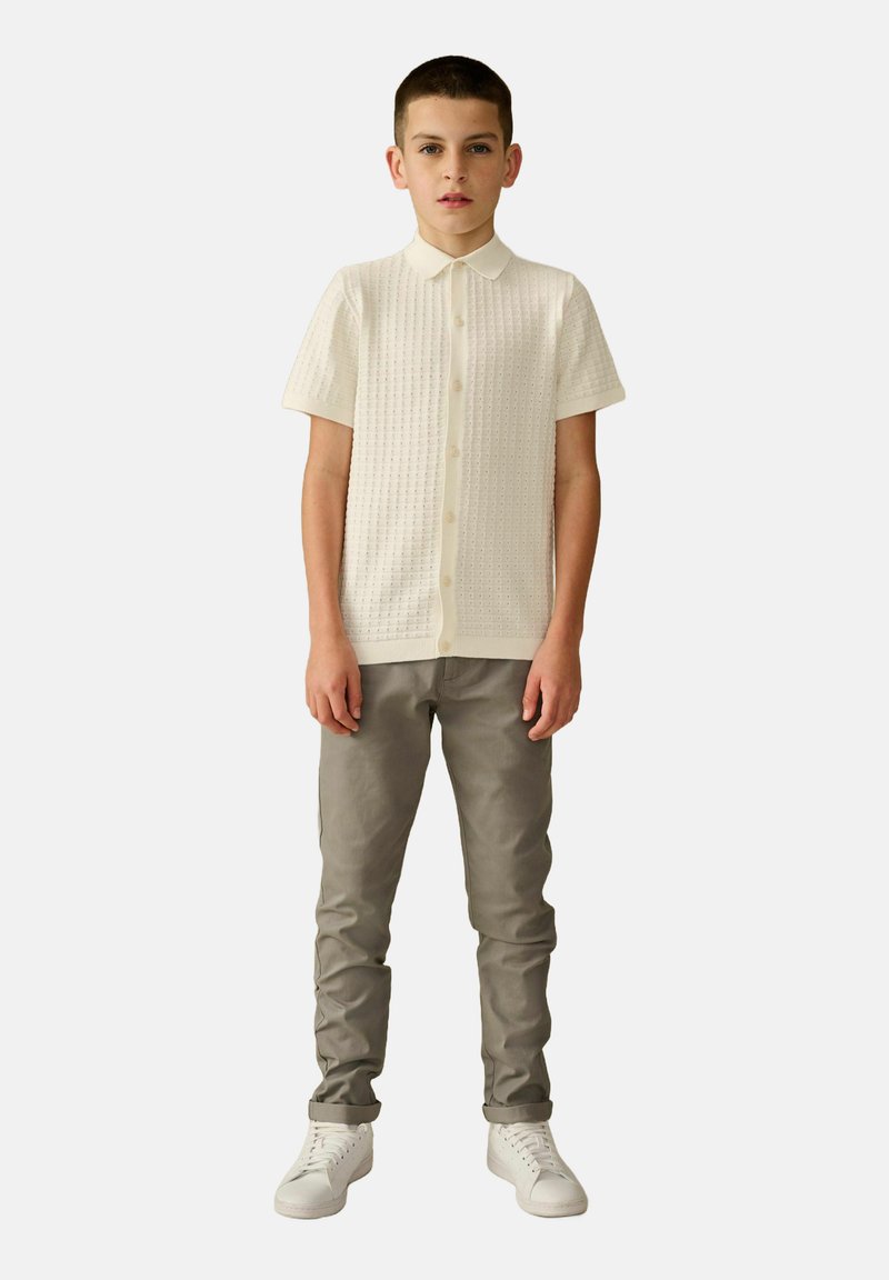 Chemise à manches courtes, crème, avec un tissu texturé, associée à un pantalon gris slim-fit et des baskets blanches.