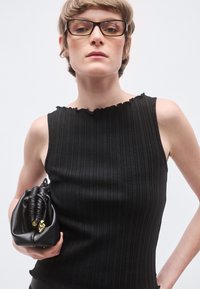 Μαύρο αμάνικο τοπ με ριμπ ύφανση και λαιμόκοψη με κυματιστό σχέδιο, συνδυασμένο με μαύρο δερμάτινο clutch με συγκεντρωμένη υφή και χρυσές λεπτομέρειες.