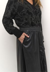 Sort tekstureret sweater med perlemønster kombineret med en højталjet skør fra kunstlæder i sort. Elastisk talje og sidelomme synlig.