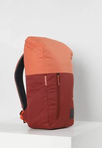 Mochila roja y naranja con la parte superior redondeada, cuenta con un bolsillo frontal con cremallera, tejido texturizado y correas de malla negras. Acentuada con un parche de logo.