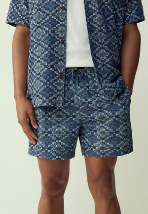 Kurzärmeliges Hemd mit Knöpfen und passende Shorts in Dunkelblau mit geometrischem Muster. Der Stoff hat eine strukturierte Oberfläche und Kordelzugdetails.