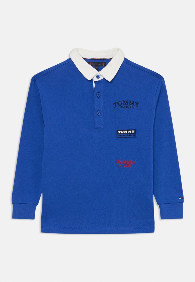Polo bleu à manches longues avec col blanc, comportant des broderies "TOMMY HILFIGER" et des patchs de logo. Patte de boutonnage et détails au niveau des poignets.