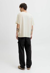 Světle béžové oversize tričko s kulatým výstřihem, v kombinaci s černými cargo kalhotami se bočními kapsami, nošené s béžovými slip-on botami.