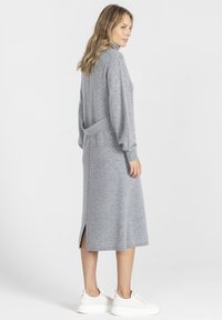 Szara dzianinowa sukienka z wysokim kołnierzem, długimi rękawami i wiązaniem w talii. Midi z bocznymi rozcięciami, w połączeniu z białymi sneakersami.
