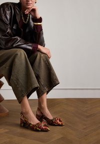 Slingback schoenen met puntige neuzen, paars en geel bloemenpatroon, blokhakken, gecombineerd met brede olijfgroene denimbroek.