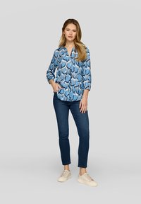 Helles blaues langärmliges Hemd mit geometrischem Muster, kombiniert mit dunklen Jeans und hellen Sneakers. Lässiger Schnitt und Knopfverschluss.