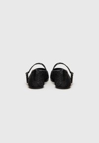 Sandales noires avec une tige en textile tissé et un talon en cuir lisse. Sangle arrière avec boucle réglable pour un maintien sécurisé.