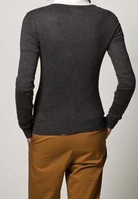 Dunkelgrauer, körpernaher Pullover mit langen Ärmeln und rundem Halsausschnitt, kombiniert mit beigen Hosen, von hinten gezeigt. Strukturierter Strickstoff.