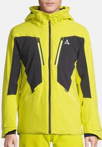 Limegrüner und schwarzer wasserdichter Anorak mit Kapuze, mit kantigem Design, Reißverschlusstaschen und kontrastierenden Akzenten.