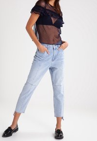 Top in rete a pois navy con maniche a volant abbinato a jeans a vita alta azzurri chiari con taglio dritto e orlo grezzo. Mocassini neri.