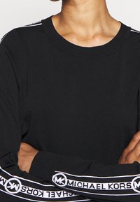 Sweatshirt noir à col rond, avec logo blanc et rayures sur les manches. Matière en coton doux, poignets côtelés et coupe décontractée.