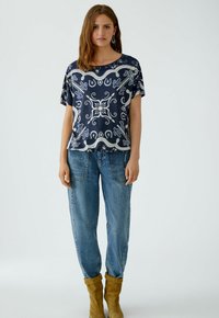Blouse à motif marin avec des manches courtes, associée à un jean bleu clair ample et des bottines en daim jaune.