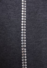 Mörkgrått tyg med en vertikal rad av metalliska nitar som tillför textur och visuella detaljer, löpande ner längs mitten.