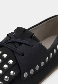 Μαύρο σουέντ παπούτσι με λεπτομερές σχέδιο με φούντες και μεταλλικά τρουκ κατά μήκος της άκρης. Διαθέτει κλείσιμο με κορδόνια και λείο εσωτερικό.