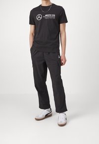 Czarna koszulka z białym nadrukiem logo, w połączeniu z czarnymi spodniami cargo z kieszeniami oraz białymi sneakersami z gumowymi podeszwami.