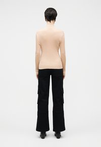 Haut beige ajusté à manches longues avec un design texturé côtelé. Associé à un pantalon cargo évasé noir avec poches latérales et une finition lisse.