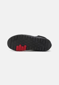 Semelle de chaussure noire avec motifs de bande de roulement hexagonaux et linéaires, avec des accents de grip texturés rouges près de la boule du pied.