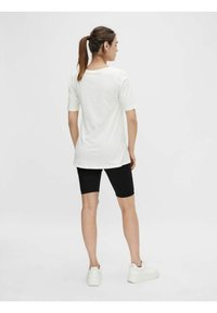 Camicia bianca a maniche corte, vestibilità ampia, abbinata a pantaloni ciclistici neri. La modella indossa sneakers bianche. Design semplice e minimalista senza motivi.