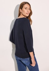 Marineblauwe longsleeve top met een ronde halslijn en een ontspannen pasvorm, gecombineerd met blauwe jeans. Soepele stof en minimale naden op de achterkant.