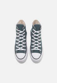 Tenisky typu high-top v tyrkysové plátně s bílými tkaničkami, černými gumovými doplňky a zaoblenou bílou špičkou. Zapínání na tkaničky a zesílené švy.