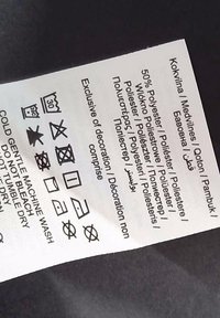 Étiquette d'entretien textile avec icônes pour le lavage, le séchage et la composition du tissu, présentant un fond blanc avec des symboles et du texte imprimés en noir.