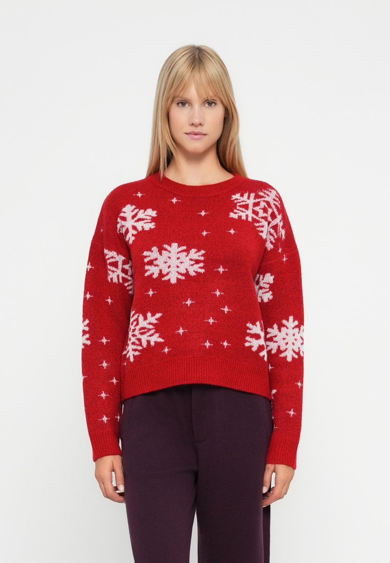 Pull en tricot rouge avec des motifs de flocons de neige et d'étoiles blancs, col rond et design court. Texture douce avec un ourlet côtelé.