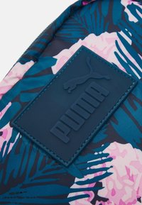 Zaino con motivo floreale in turchese, rosa e blu navy. Presenta un'applicazione in gomma testurizzata blu navy con il logo Puma e lettere in rilievo.