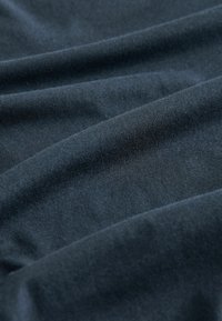 Tumed sinine kangas sujuva, veidi tekstureeritud pinnaga, millel on voldid ja ühtlane, peene ribiline muster.