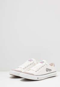 Canvas-Sneaker in Weiß mit hellbraunen Akzenten, flachen Schnürsenkeln, Logodetail an der Seite und Gummisohle. Rundes Zehendesign.