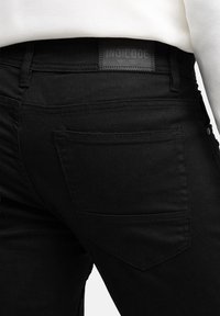 Jeans neri con una vestibilità slim, dotati di tasca posteriore, etichetta in pelle con la scritta "INDICODE" e dettagli di cucitura sottili.