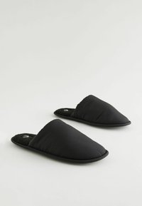 Chaussons en tissu noir avec une texture matelassée et un design à dos ouvert. Doublure intérieure douce et moelleuse pour le confort, soutenue par une semelle plate.